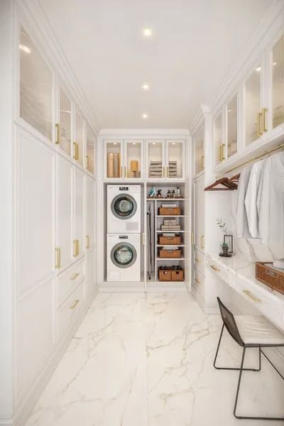 Elegant white laundry room with stacked washer/dryer, built-in cabinets, marble floor, and a small desk.