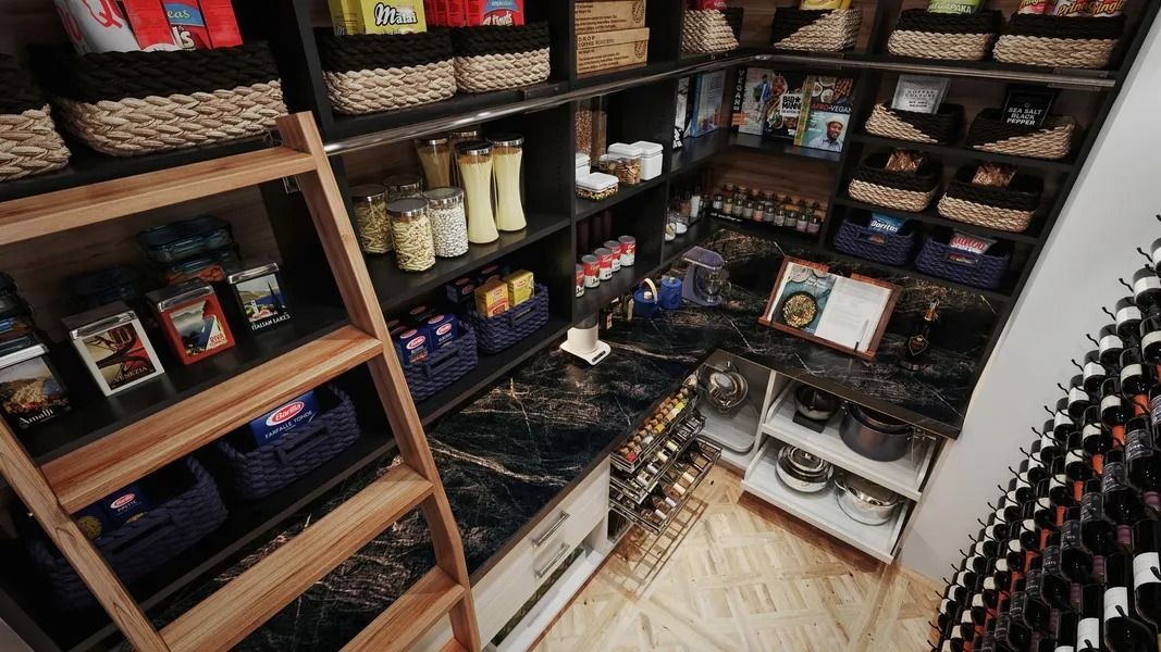 Well-stocked pantry with shelves, baskets, and various food items; a ladder leans against the shelves.