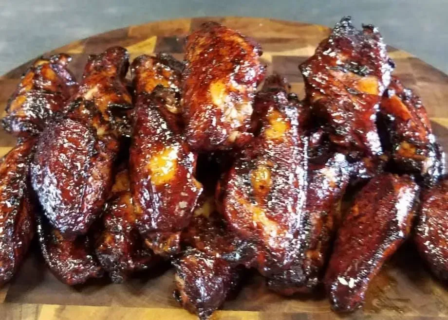 Pile of glazed chicken wings on a wooden cutting board; dark brown with glossy sauce.