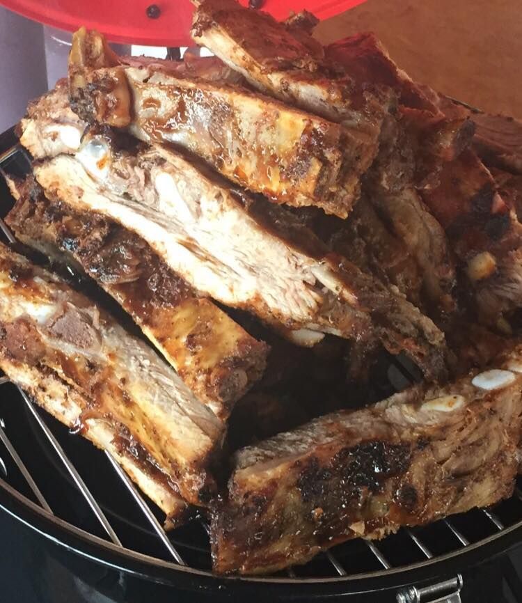 Grilled ribs piled on a barbecue grill. Dark brown, with some bones visible.
