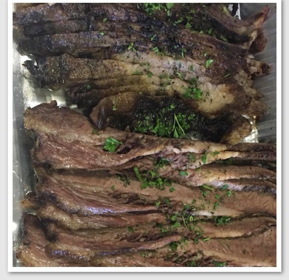 Sliced, cooked brisket with dark bark and sprinkled parsley, served in a metal tray.