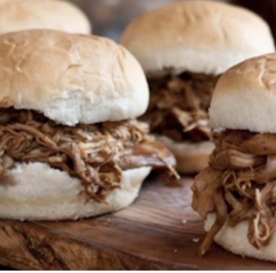 Pulled pork sandwiches on white buns, wooden board.