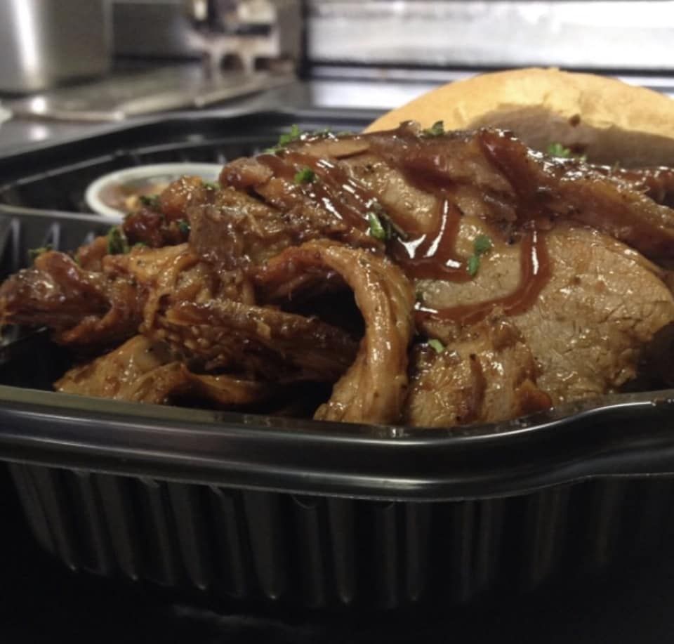 Pulled pork sandwich in a black container, with sauce, bun, and a small sauce cup.