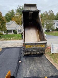 Open dump truck bed pouring fresh black asphalt onto a suburban driveway