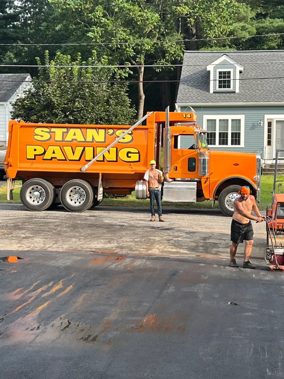 Orange Stan’s Paving truck at a roadside job site with workers standing nearby