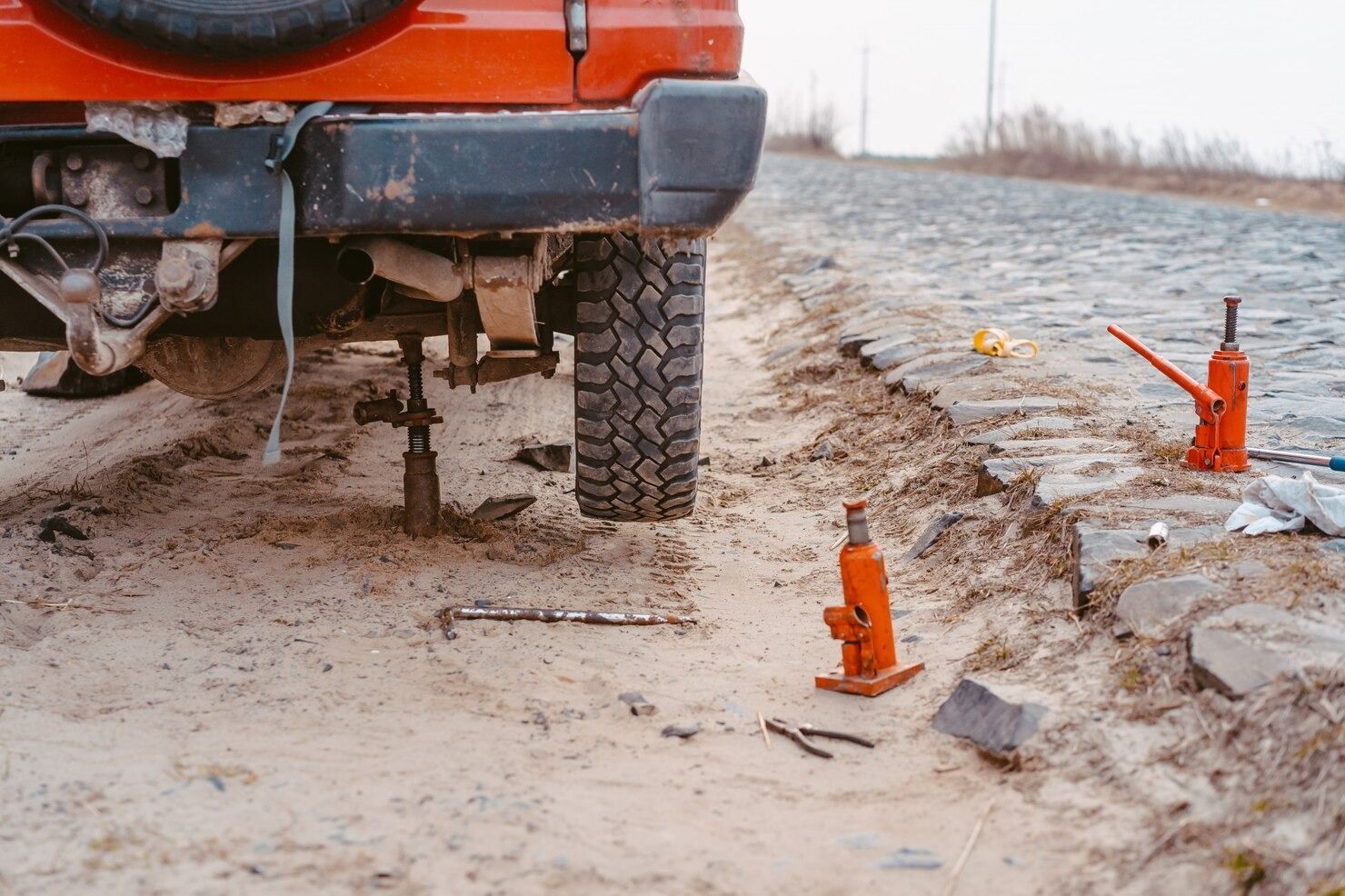 Orange vehicle on muddy roadside with orange traffic cones marking a damaged ditch