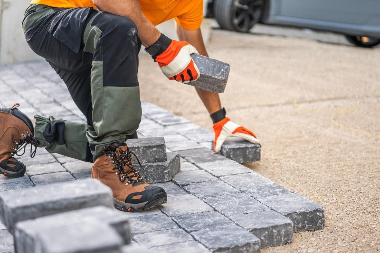 Worker laying gray paving stones on a sidewalk with a mallet and gloves