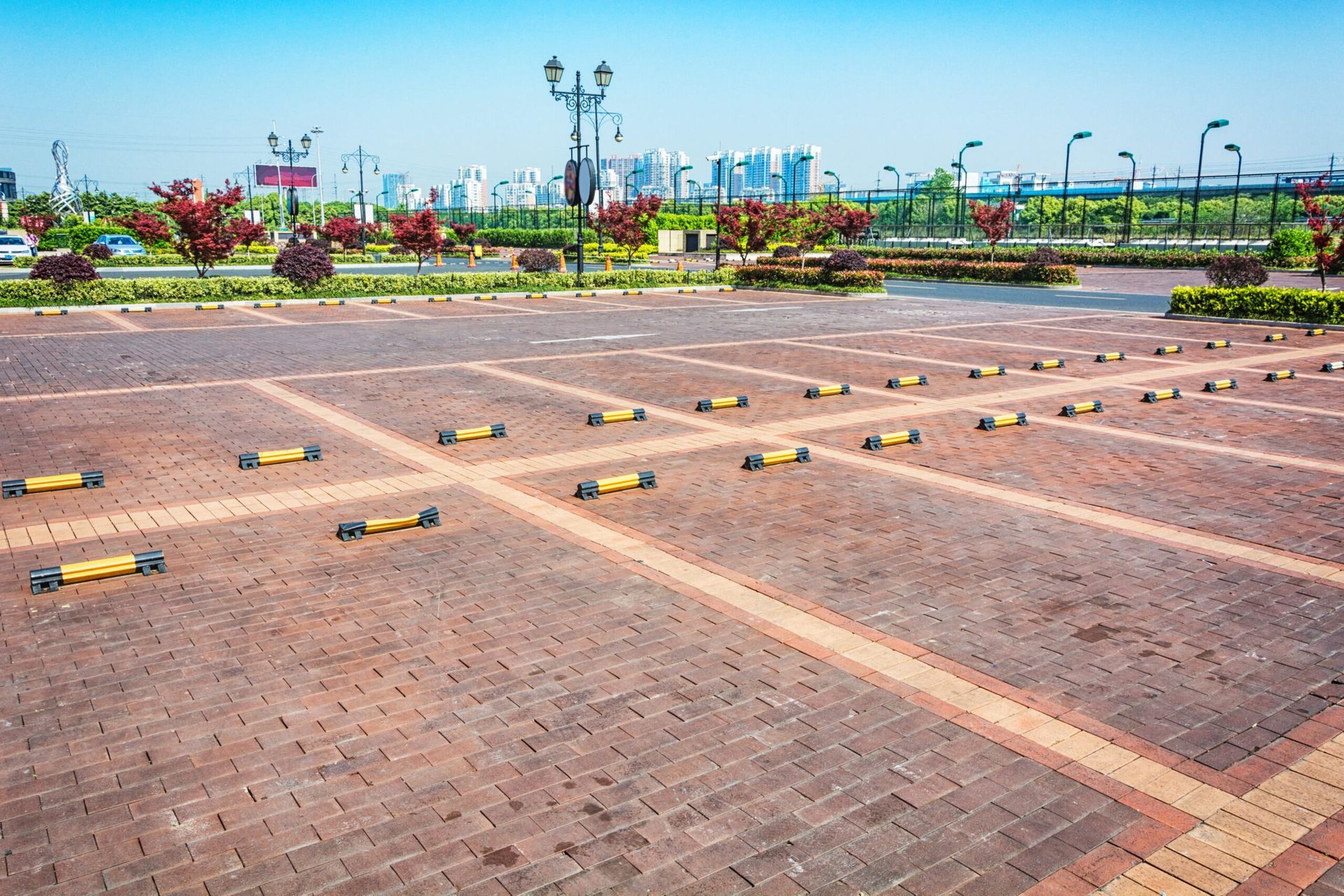 Empty brick-paved parking lot with yellow wheel stops and landscaped greenery in the background
