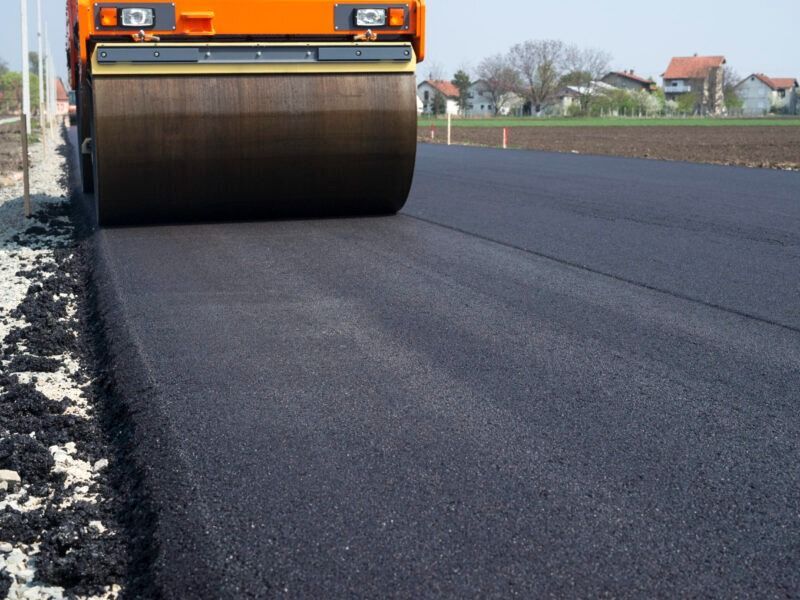 Road roller paving a dark asphalt road on a rural street