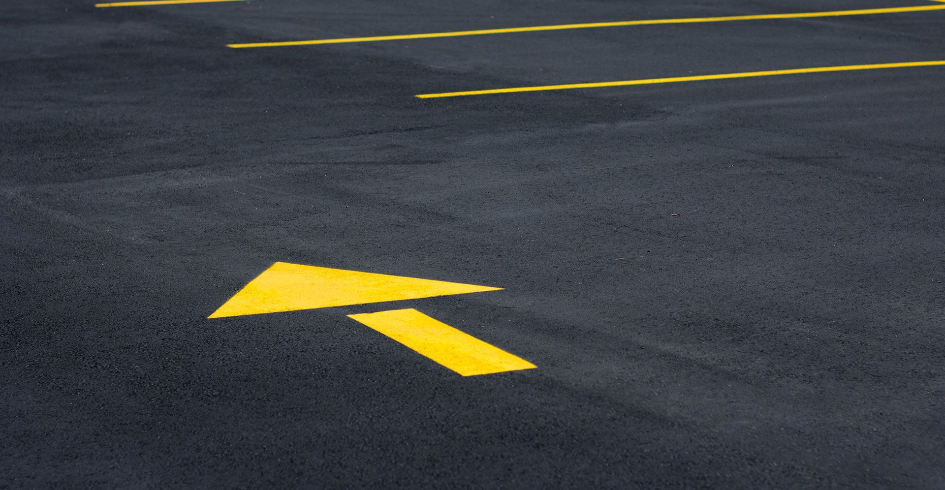 Yellow directional arrow painted on dark asphalt parking lot pavement.