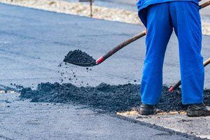 A man is using a shovel to spread asphalt on a road.