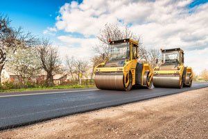 Two asphalt rollers are driving down a road.