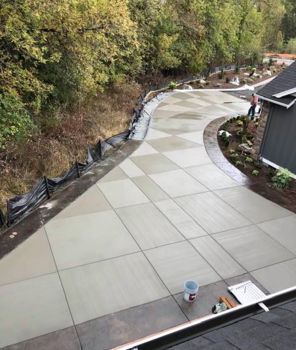 Freshly poured concrete driveway with checkered pattern, bordered by landscaping, curving up hill towards a house.