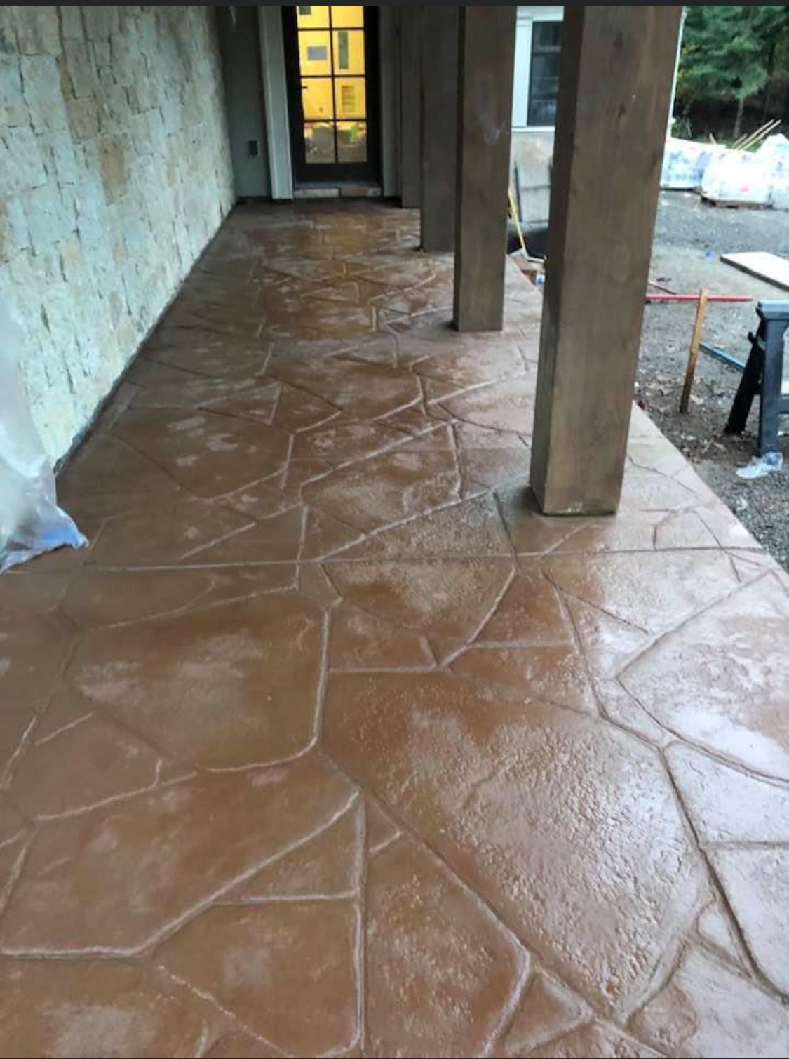 Brown, textured concrete patio with stone-like pattern, under a covered porch with stone and brown supports.