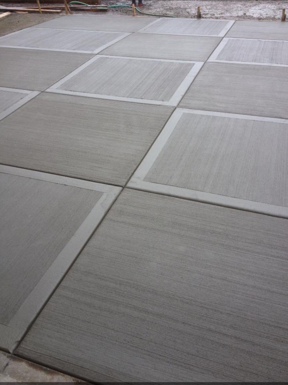 Freshly poured concrete patio with square inset design, light and dark gray hues.