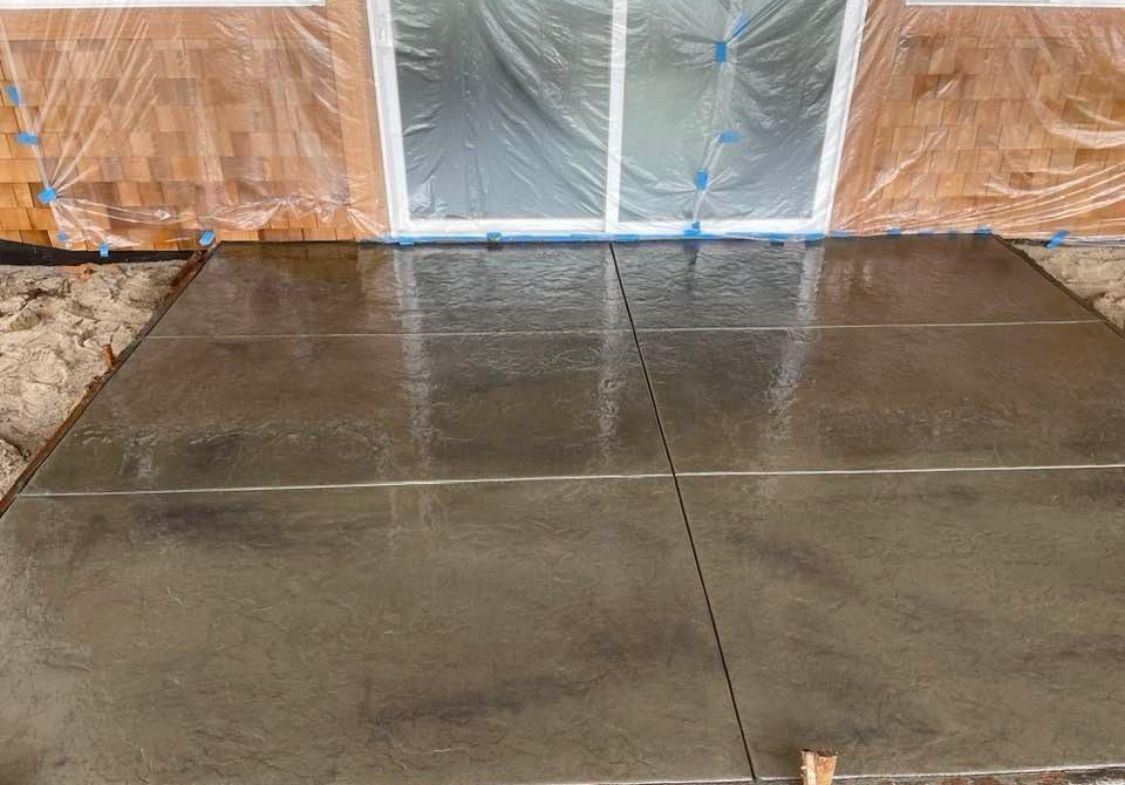 Newly poured concrete patio in front of a house; clear plastic protects the windows.