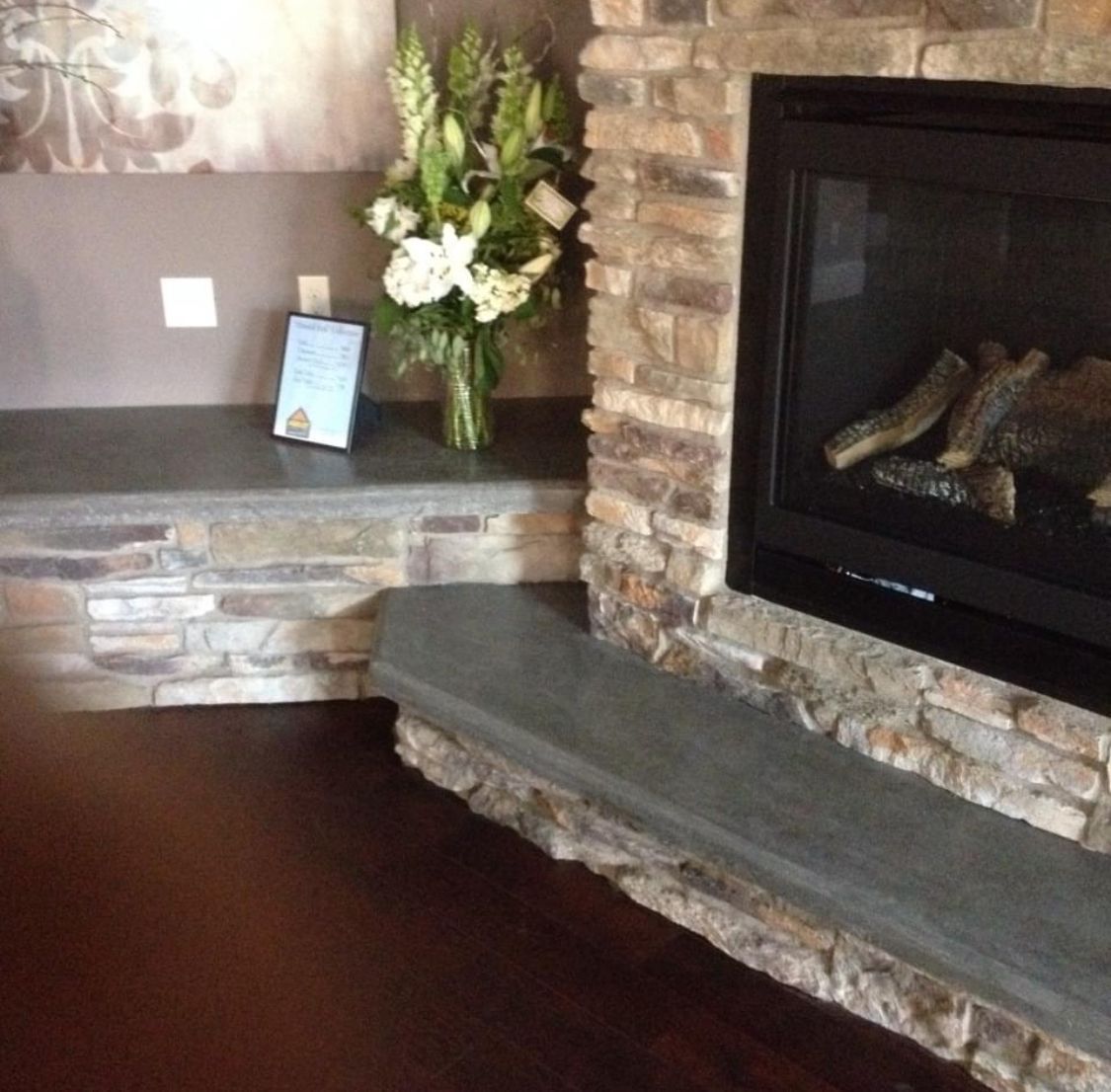 Fireplace with stone surround, dark hearth, and flowers; dark wood floor.