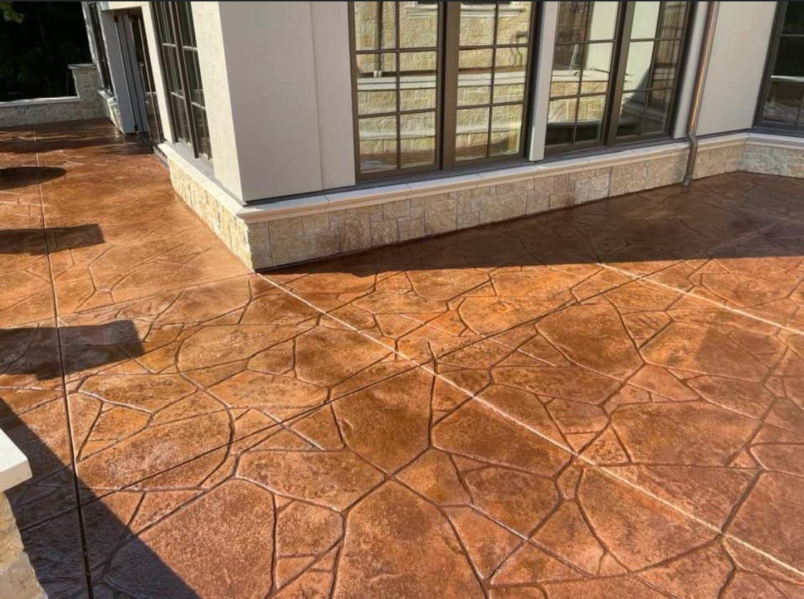 Stamped concrete patio, brown tones, near building with large windows, sunny day.