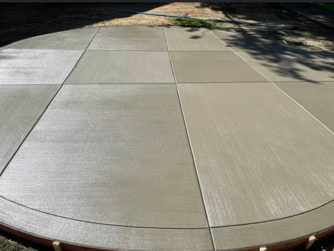 Freshly poured concrete patio, circular with straight and curved lines. Light gray with a wooden form.
