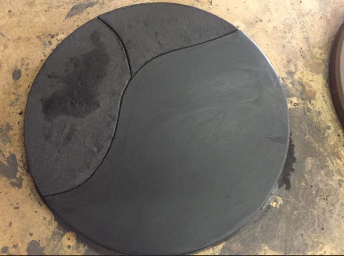 Dark grey circular object, divided into three sections by curved lines, on a light brown surface.