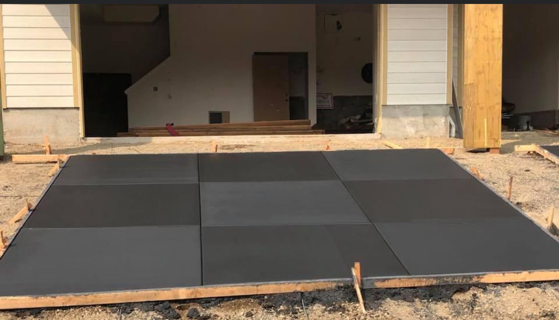 Concrete patio under construction with dark gray square tiles framed by wood.