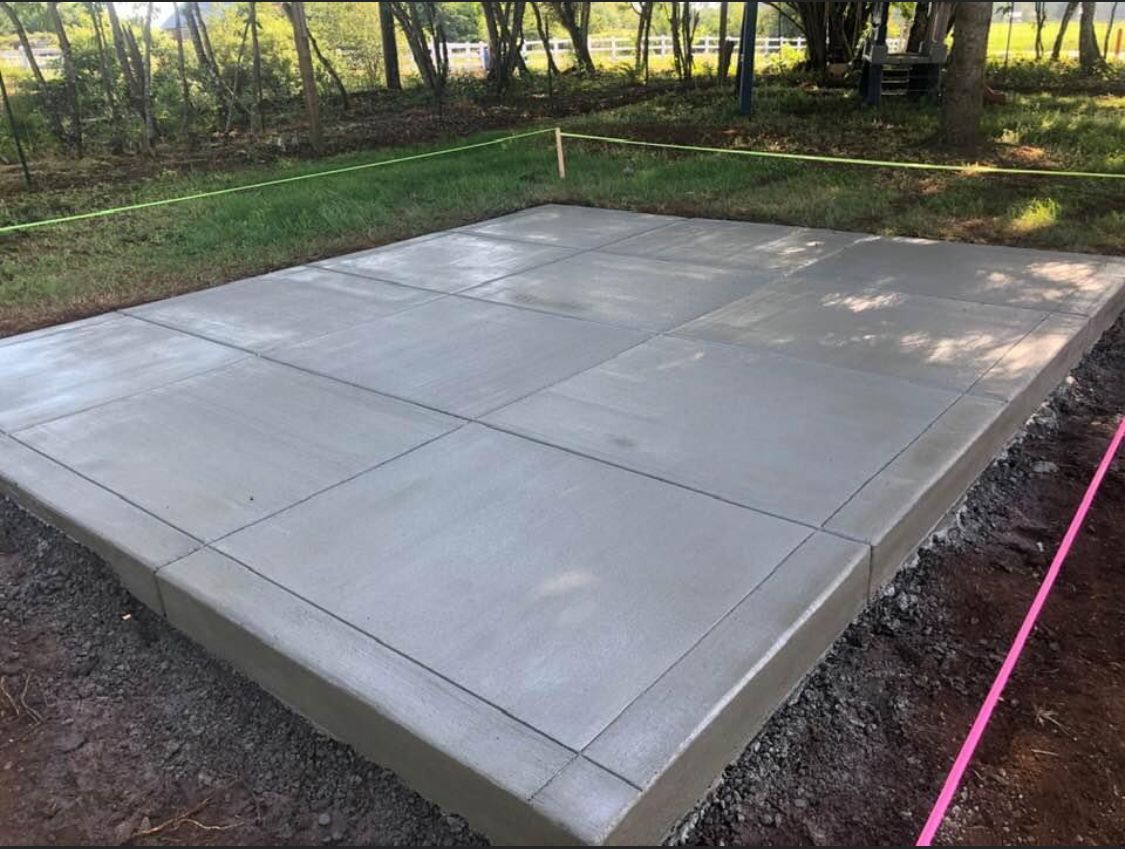 A freshly poured concrete slab with saw cuts, surrounded by dirt and grass.