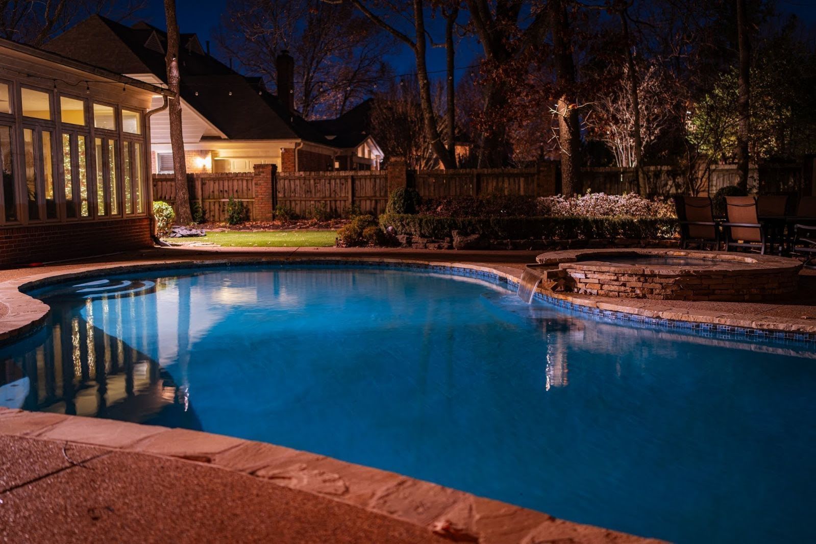 A large swimming pool is lit up at night in a backyard.