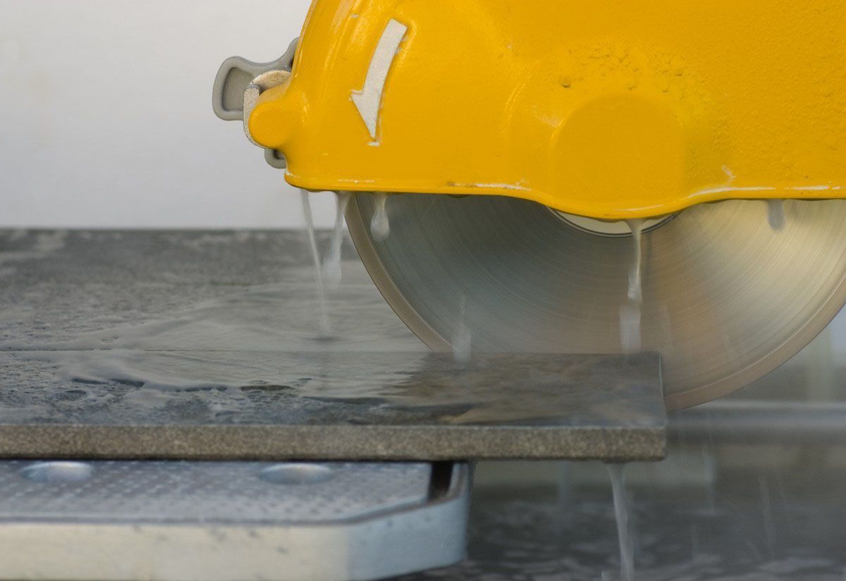 Yellow circular saw cutting a gray stone tile with water spraying