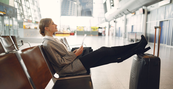 A person in a business suit sitting on the floor by a window in an airport terminal, looking distressed beside a suitcase.