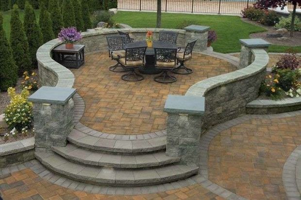 Stone patio with steps and curved wall surrounding a dining set on a brick-paved surface.