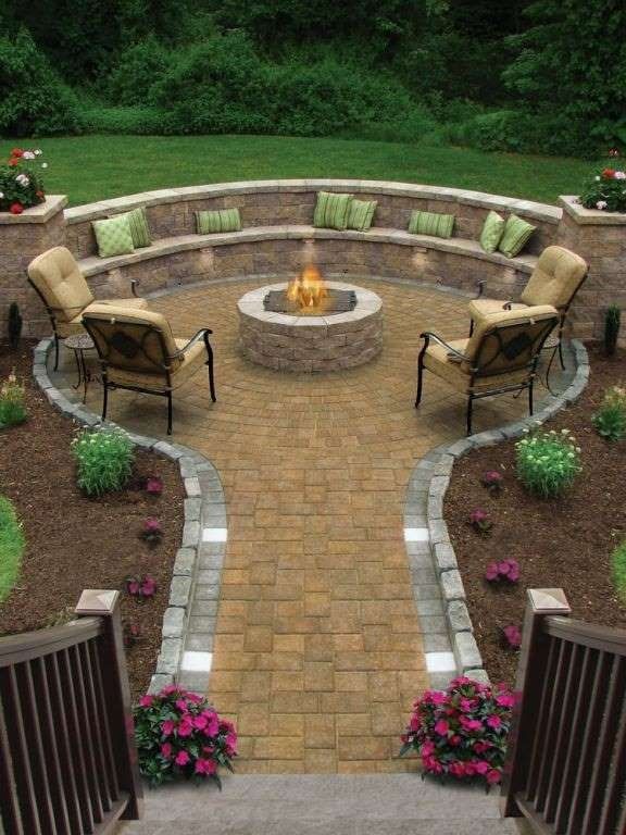 Stone patio with a fire pit, surrounded by seating, a curved wall, and lush greenery.