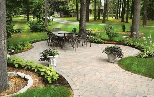Stone patio with table and chairs, surrounded by greenery and trees.