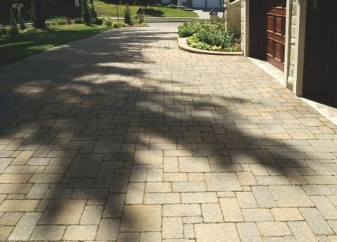 Brick paver driveway with dappled shadows leading to a garage entrance with a wooden door.