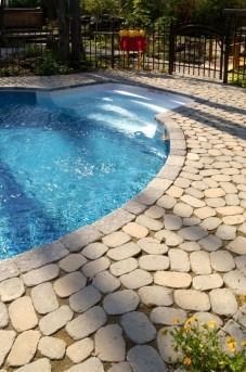 Pool with blue water and stone patio, with a wooden fence in the background.