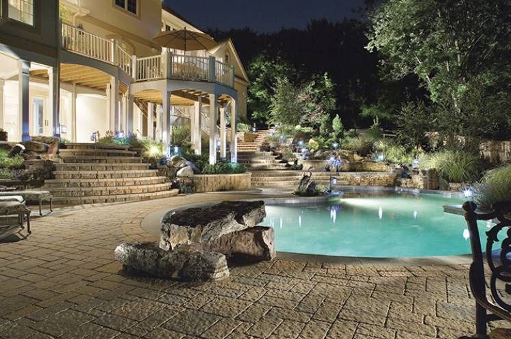 Luxury home exterior with illuminated pool and landscaping at night.