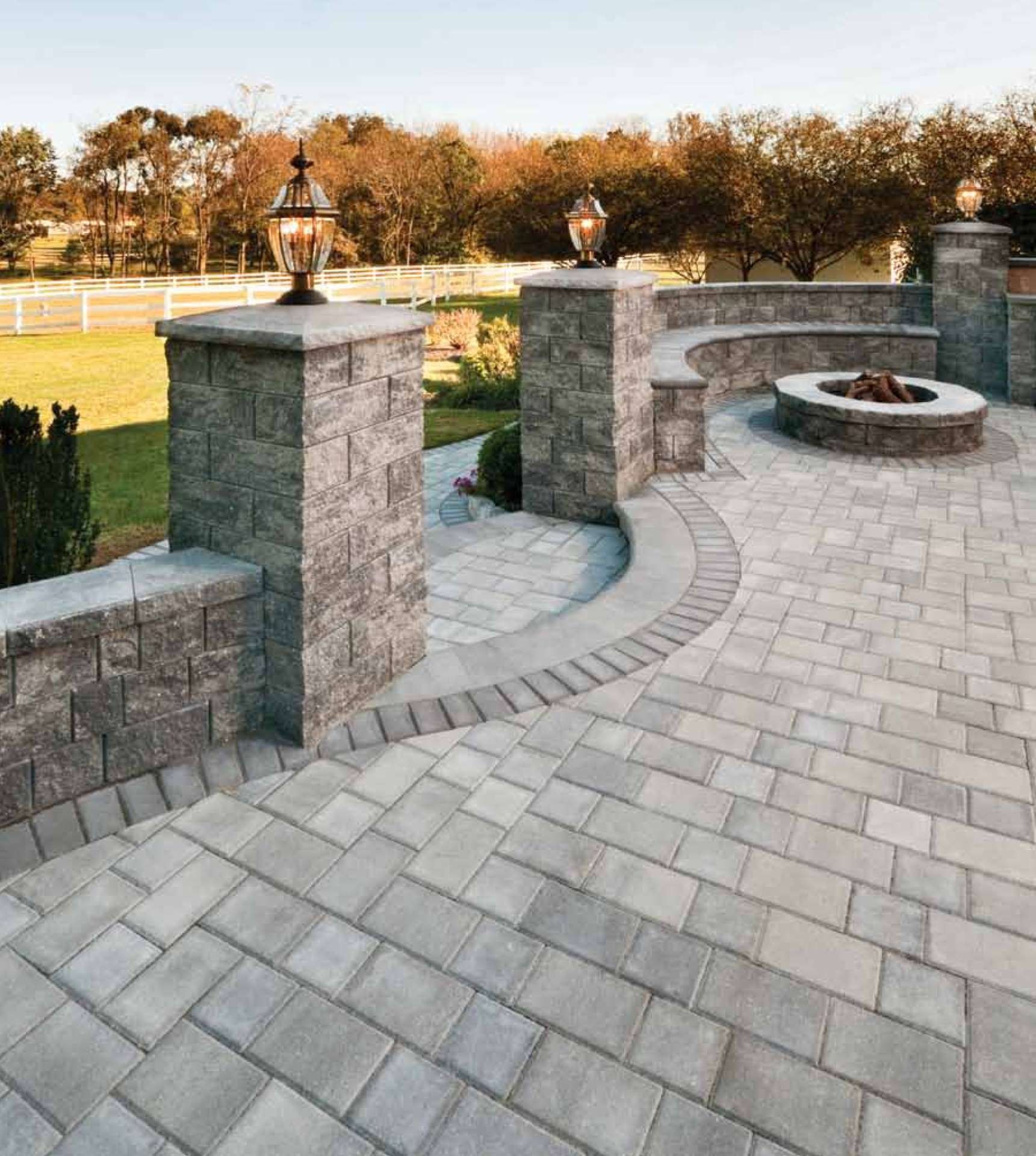 Paver patio with a curved wall, seating, and fire pit. Two stone columns with lights.