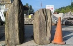 Two large, weathered stones stand upright next to an orange traffic cone, outdoors.