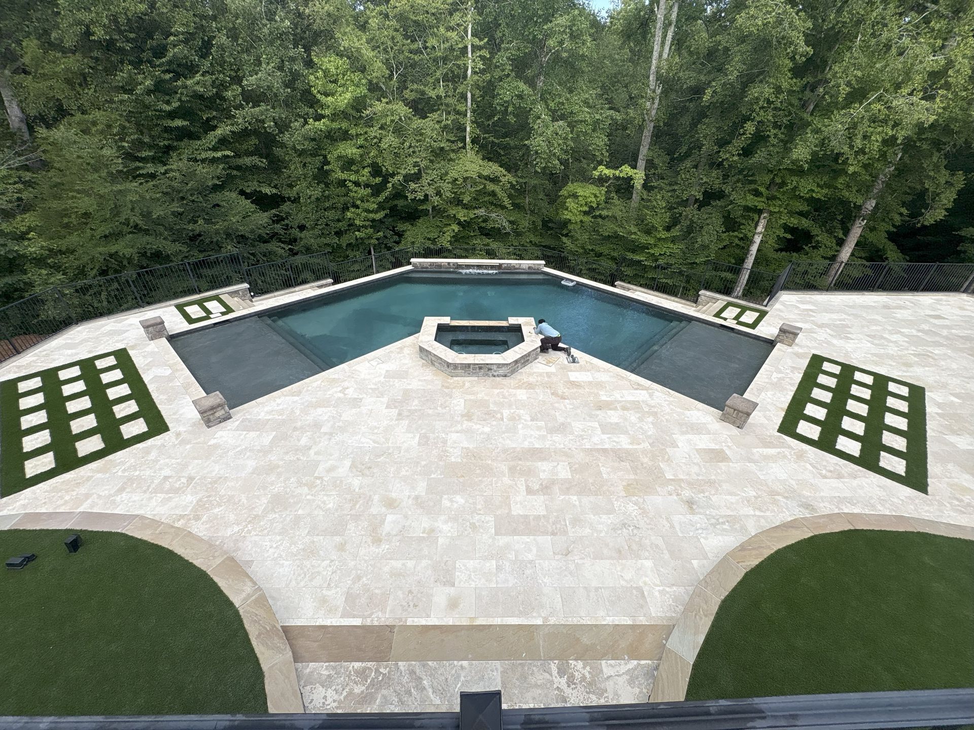 Pool deck with pool, spa, and green turf surrounded by trees.