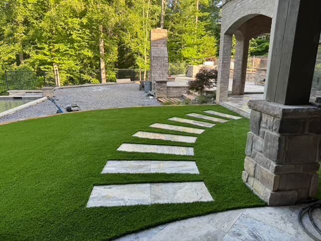 Stone pathway on vibrant green turf leading to a covered patio.