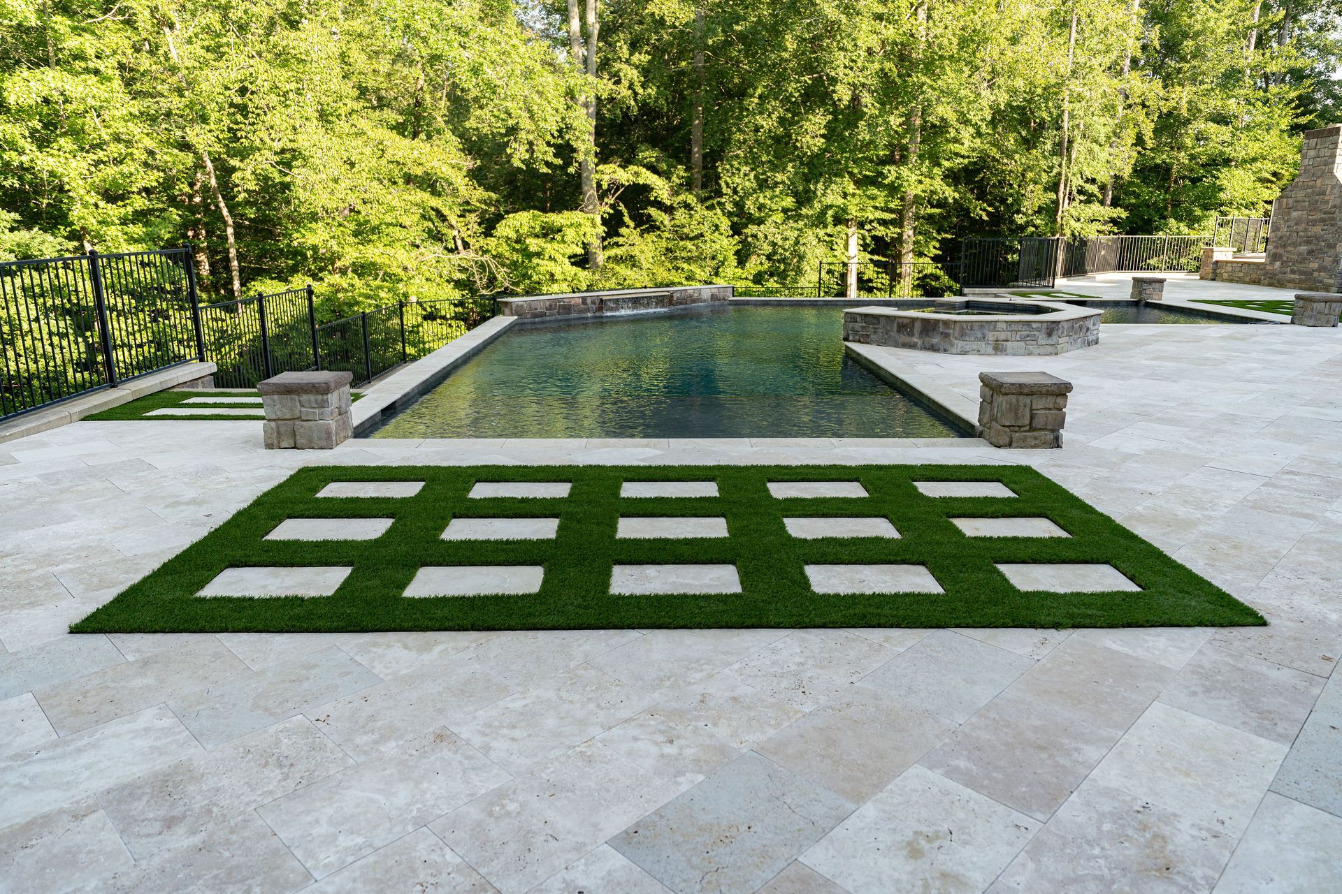 Stone patio with pool, grass squares, and forest background.
