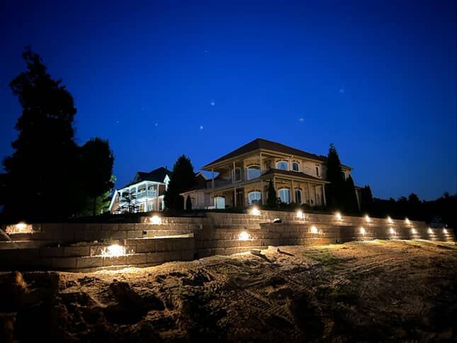 Two lit houses at night, built into a terraced hillside. Bright lights illuminate the steps.