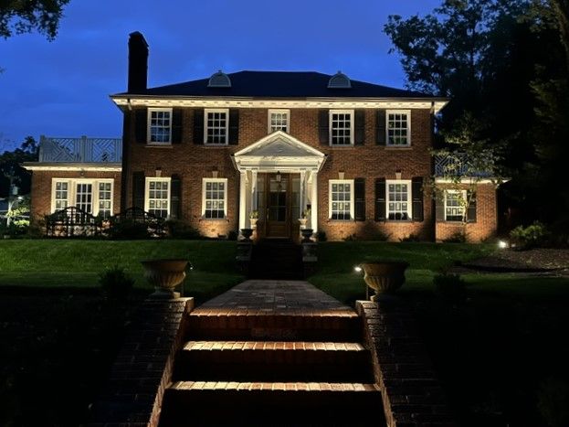 Brick house with outdoor lighting illuminating the facade and walkway. Dusk setting.