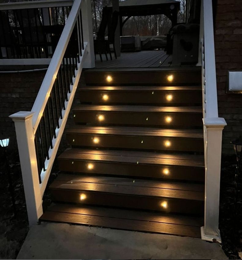 Wooden outdoor stairs with installed lighting, railing, and a deck at the top, dimly lit at night.