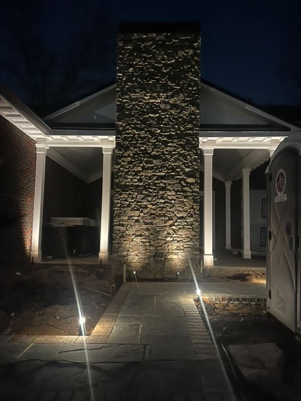 Night view of a building with an illuminated stone chimney and walkway. Uplighting highlights the textured stone and facade.