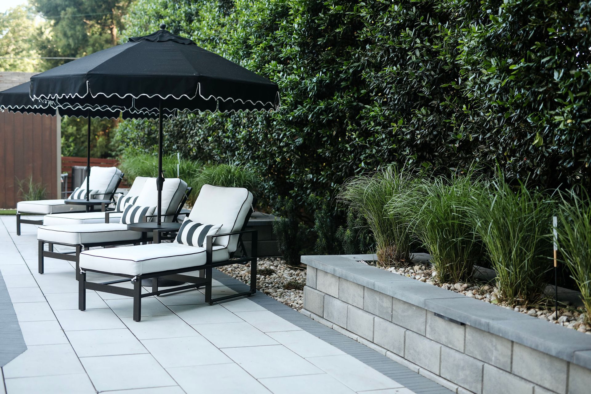 Outdoor seating area with black and white umbrellas, lounge chairs, and a raised garden bed with greenery.