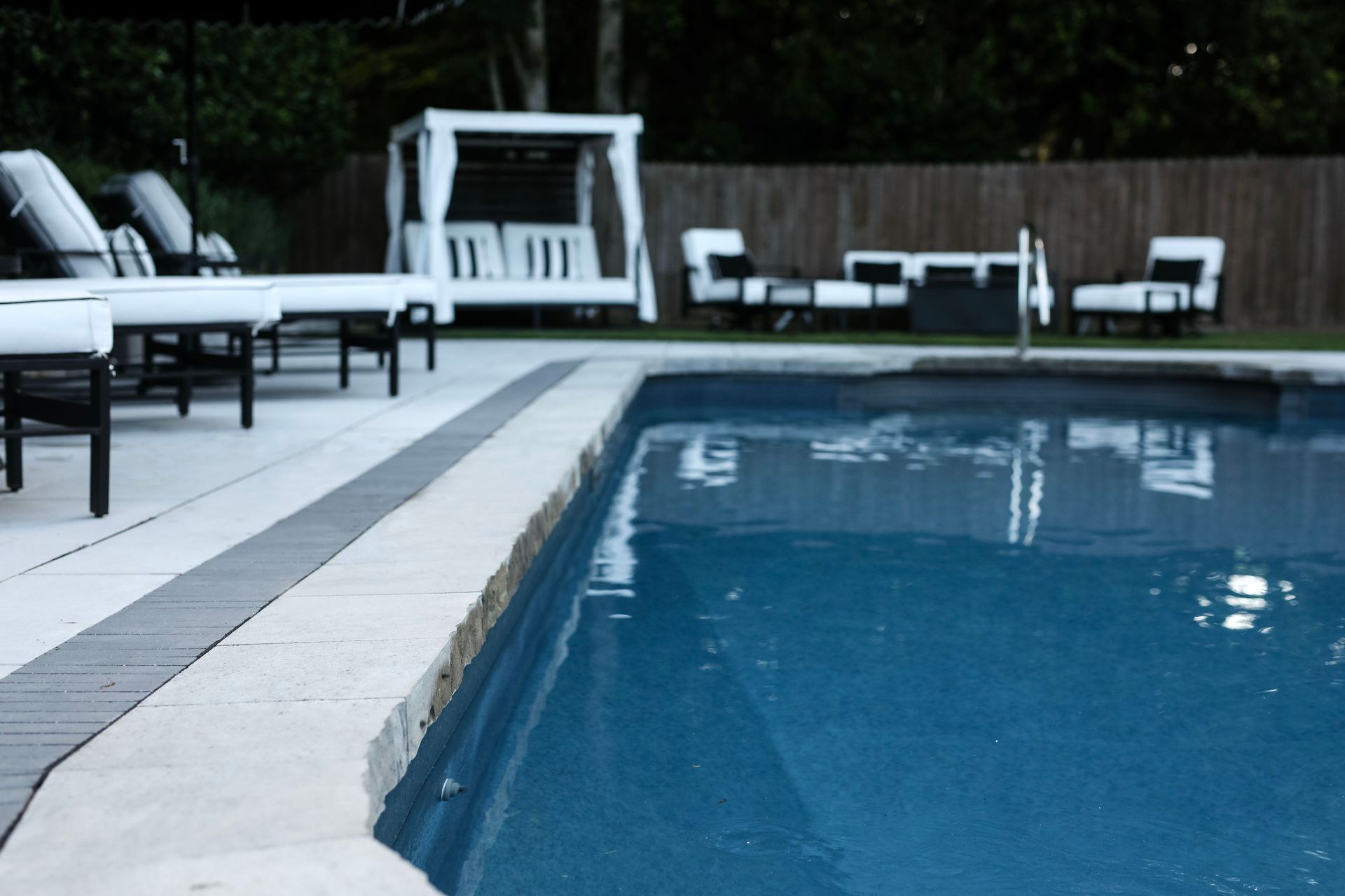 A swimming pool with surrounding lounge chairs and a gazebo, set in a backyard.