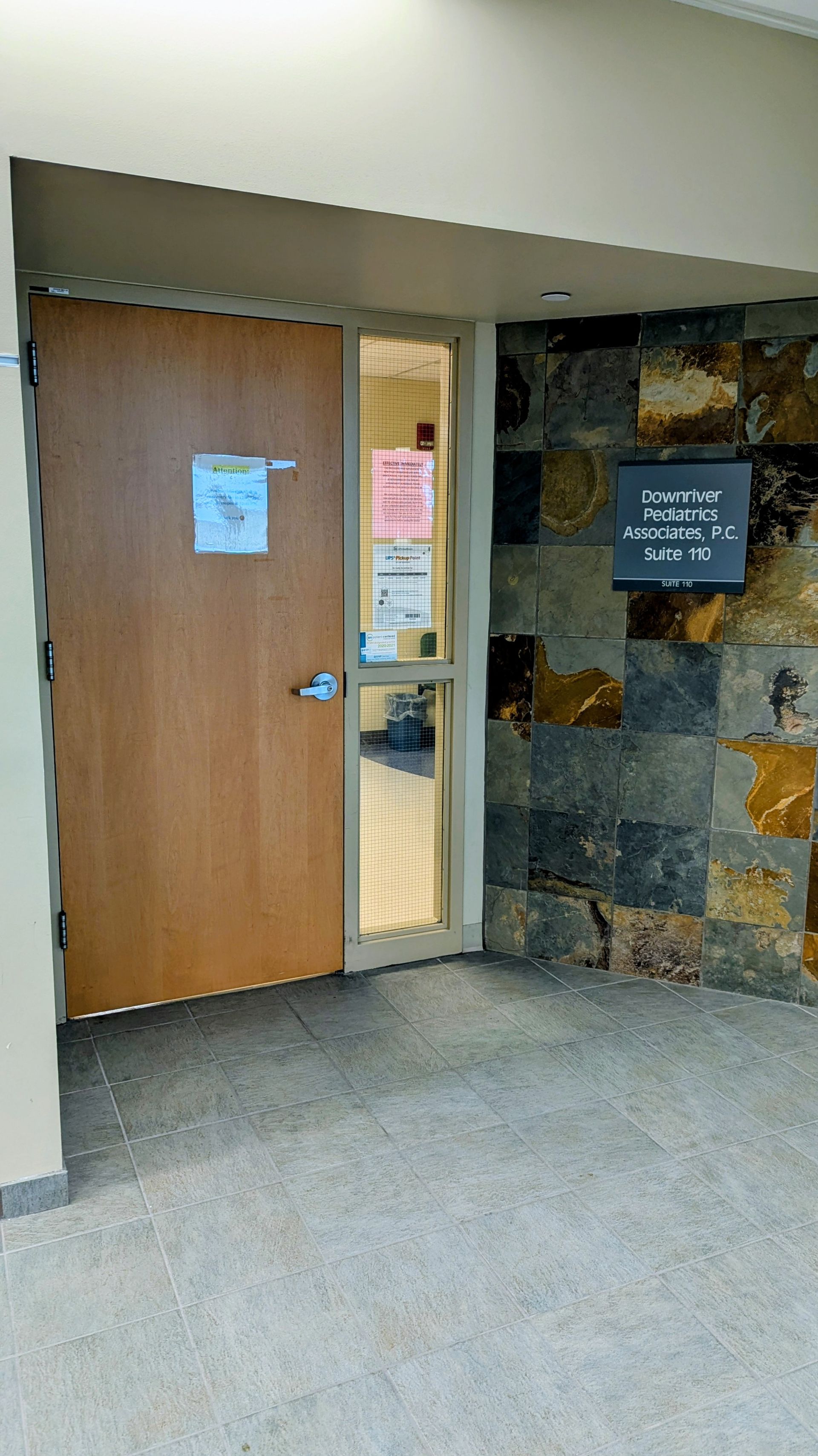 Building entrance with wooden door, stone wall, and small signs in a carpeted hallway
