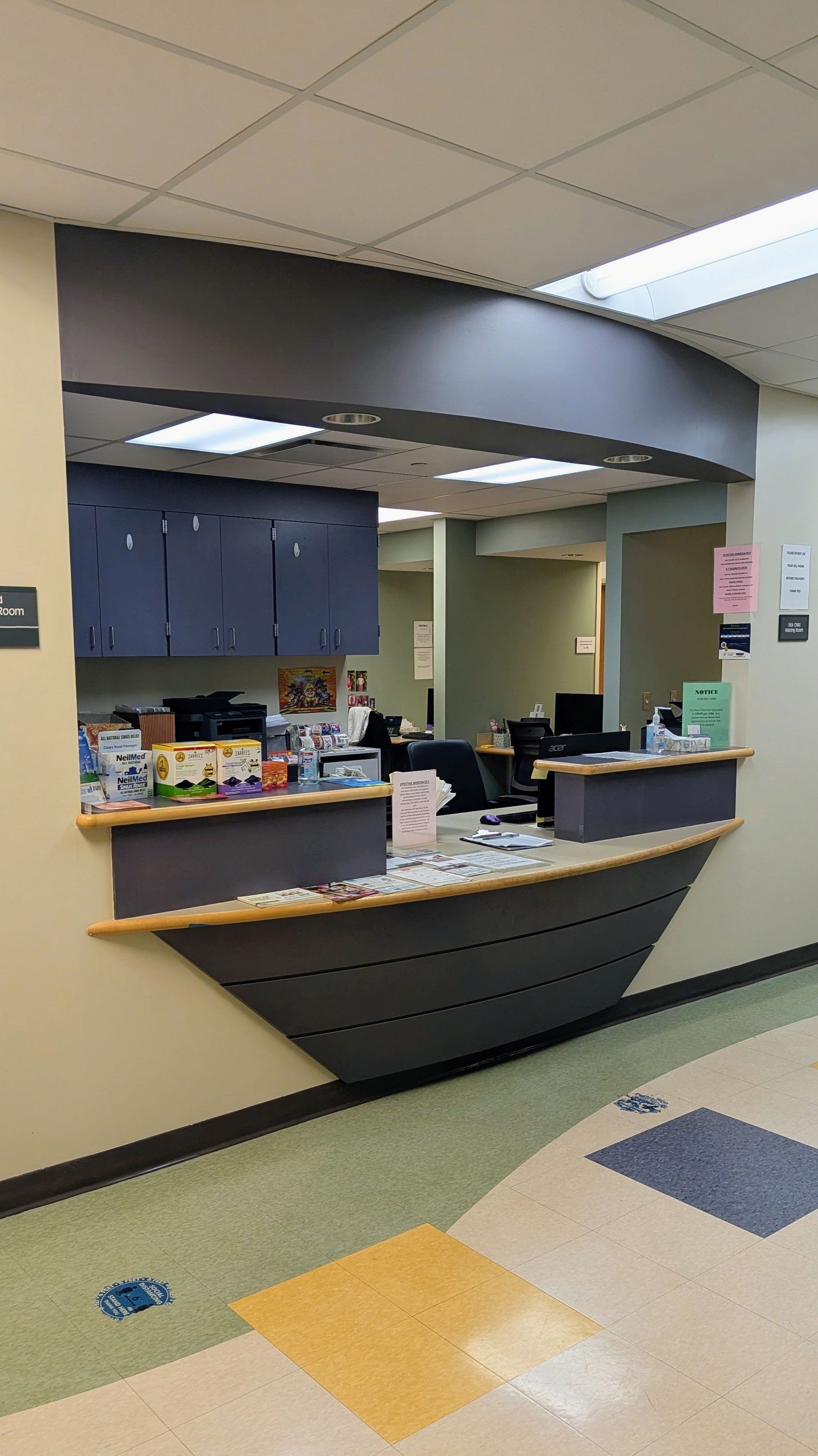 Empty reception desk in a hallway with dark cabinets, tiled floor, and a small service window.