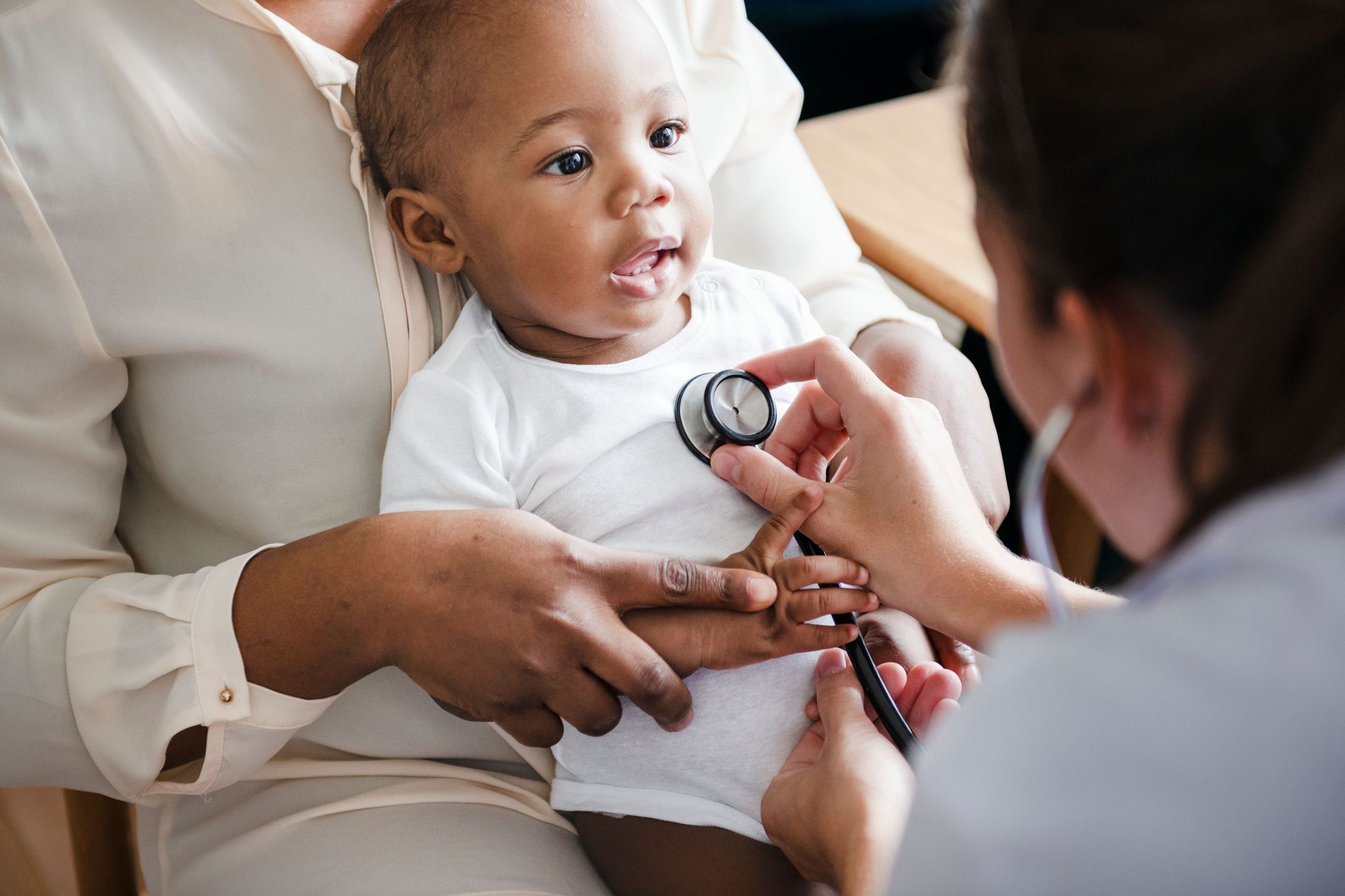 Doctor examining a baby with a stethoscope while a caregiver holds the child