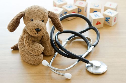 Brown stuffed dog with a stethoscope beside alphabet blocks on a table